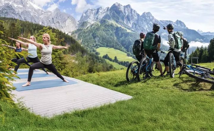 Marion beim Yoga im Freien vor einer Berglandschaft mit Radfahrern